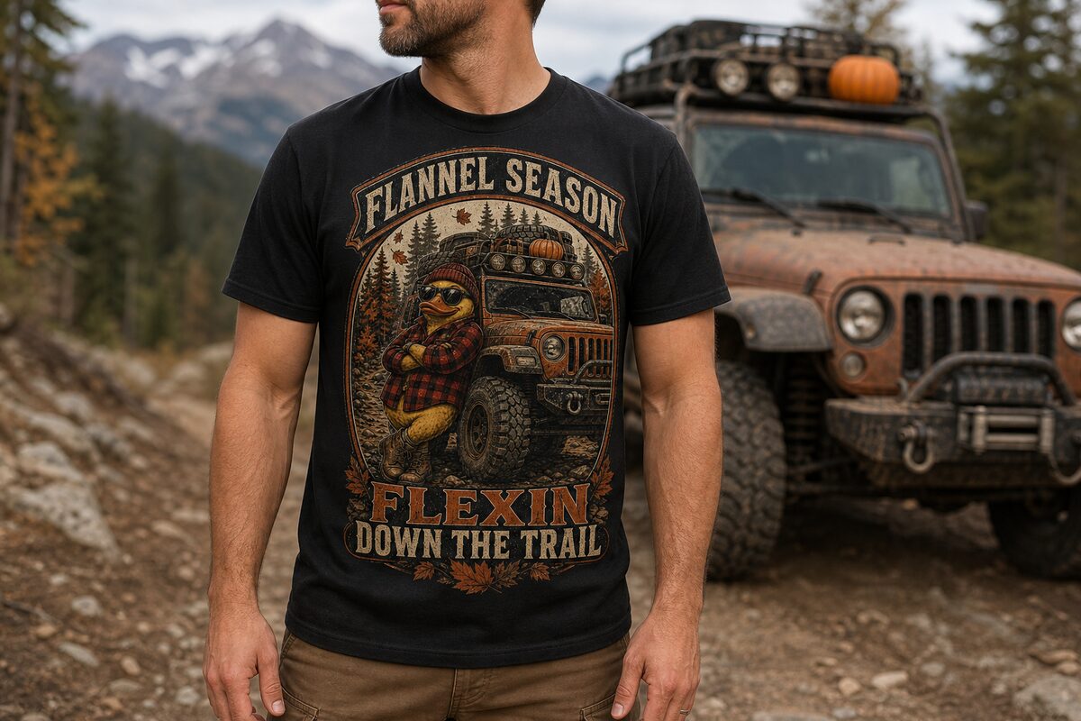 Model wearing a black tee with the FLANNEL SEASON print — a flannel-and-beanie duck leaning on an off-road rig with a pumpkin on the rack