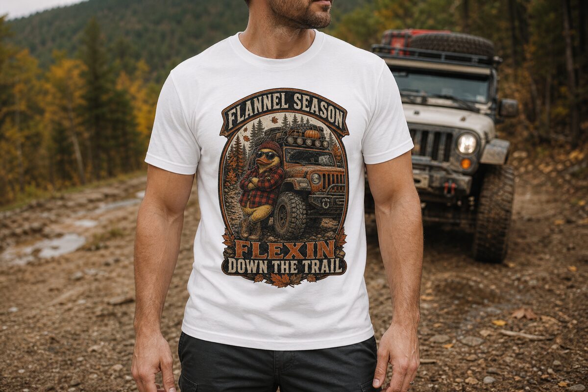 Model wearing a white tee with the FLANNEL SEASON print — a flannel-and-beanie duck leaning on an off-road rig with a pumpkin on the rack